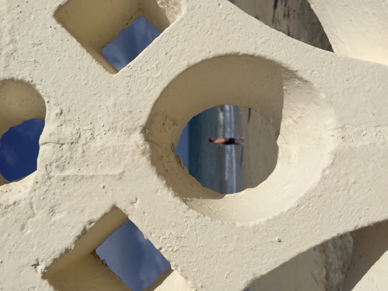 Photo of a man on the beach taken through a circular hole in the wall.